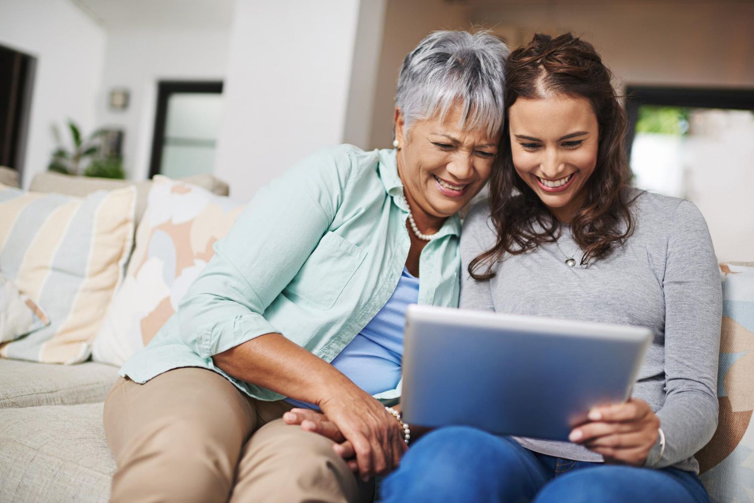 Two people smiling on a couch, using a laptop together in a bright living room