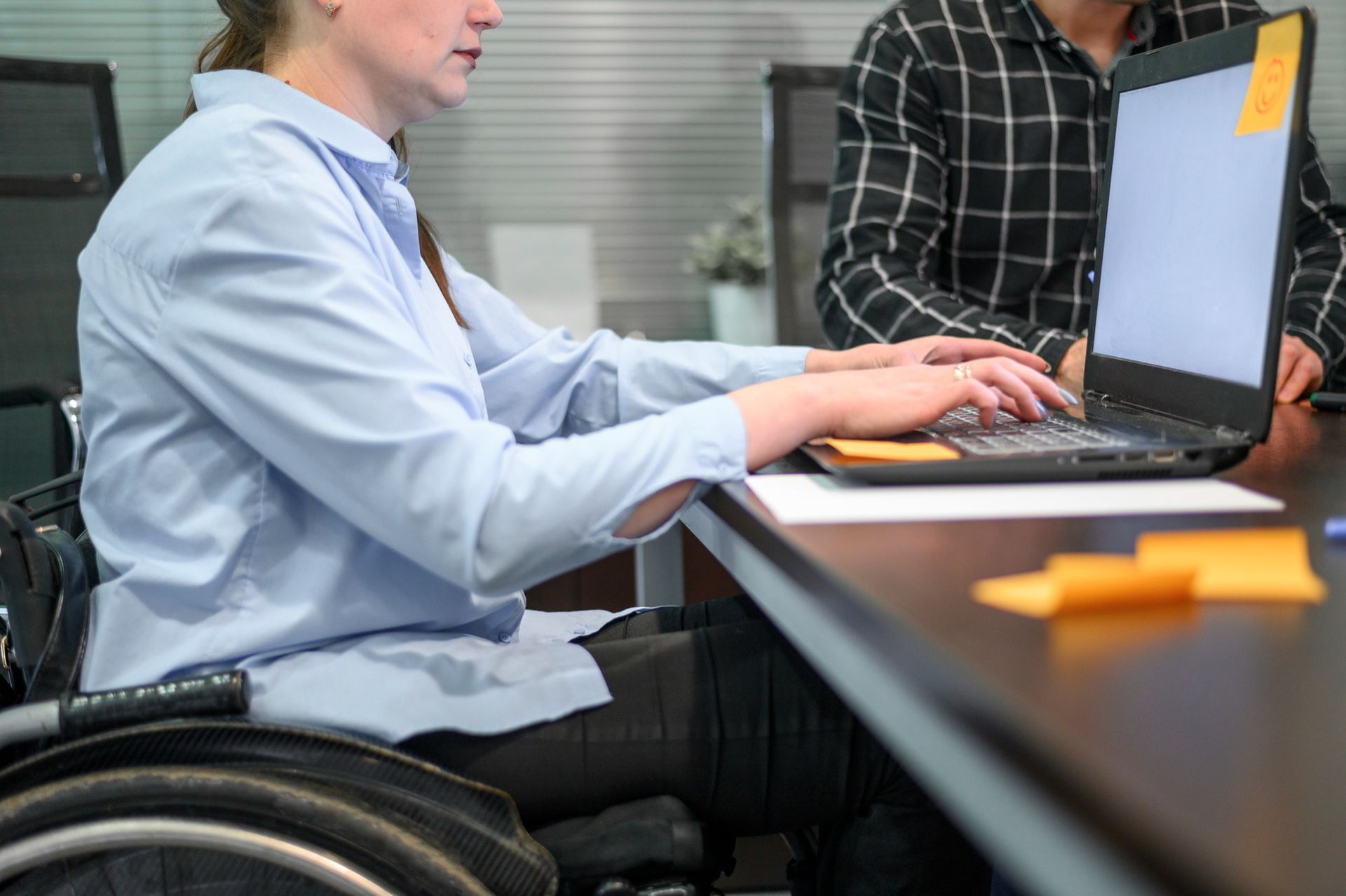 Person typing on a laptop at a conference table with orange sticky notes nearby