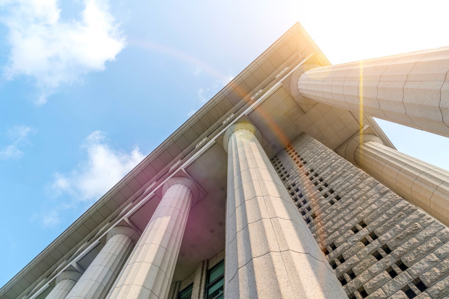 Low-angle view of a modern building with tall columns against a blue sky and sunlight