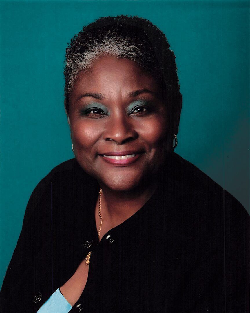Smiling portrait against a teal background, wearing a black jacket and turquoise top.