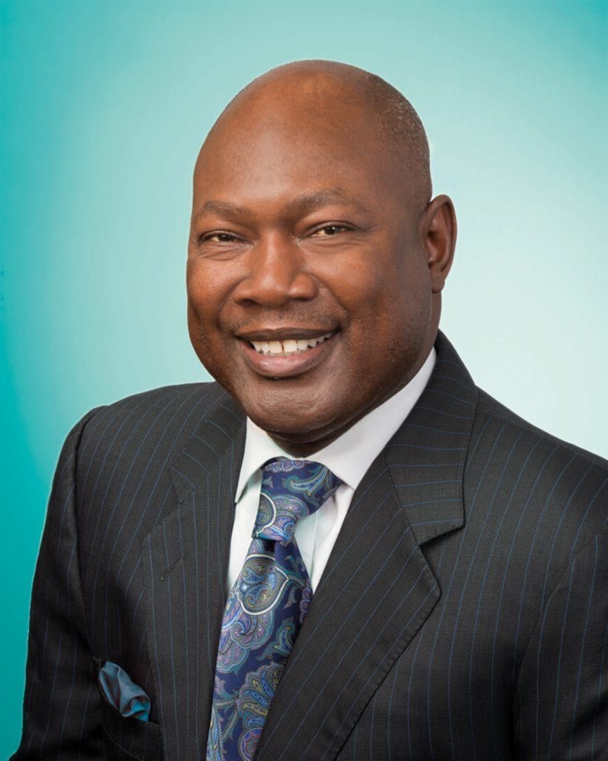 Smiling man in a dark suit and blue tie against a light blue background