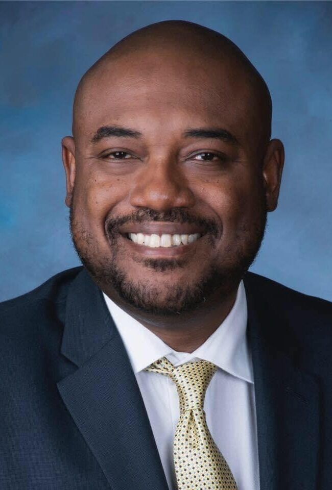 Portrait of a smiling man in a dark suit and tie against a blue background