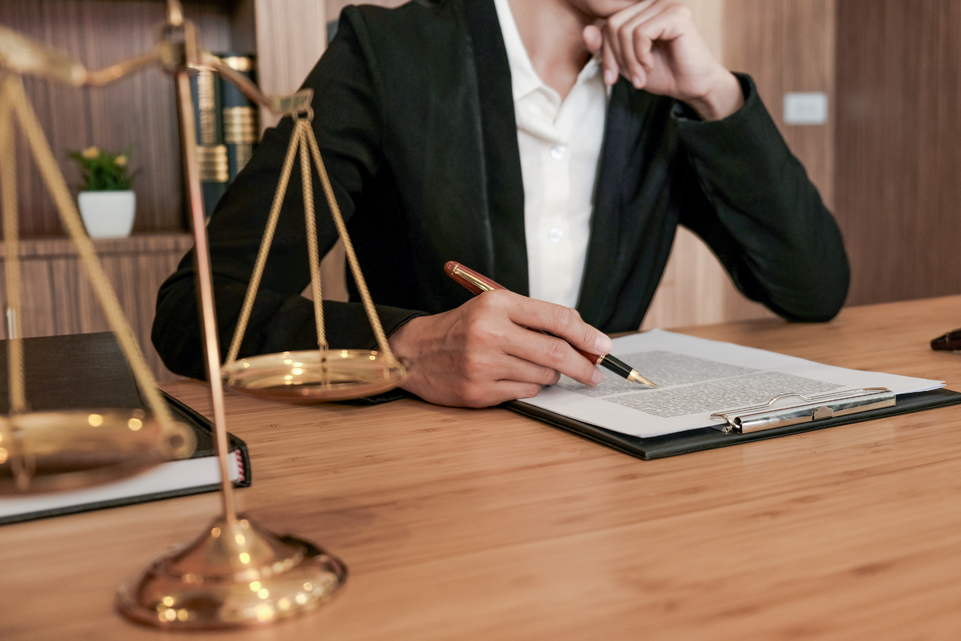 Lawyer writing at a desk beside brass scales of justice