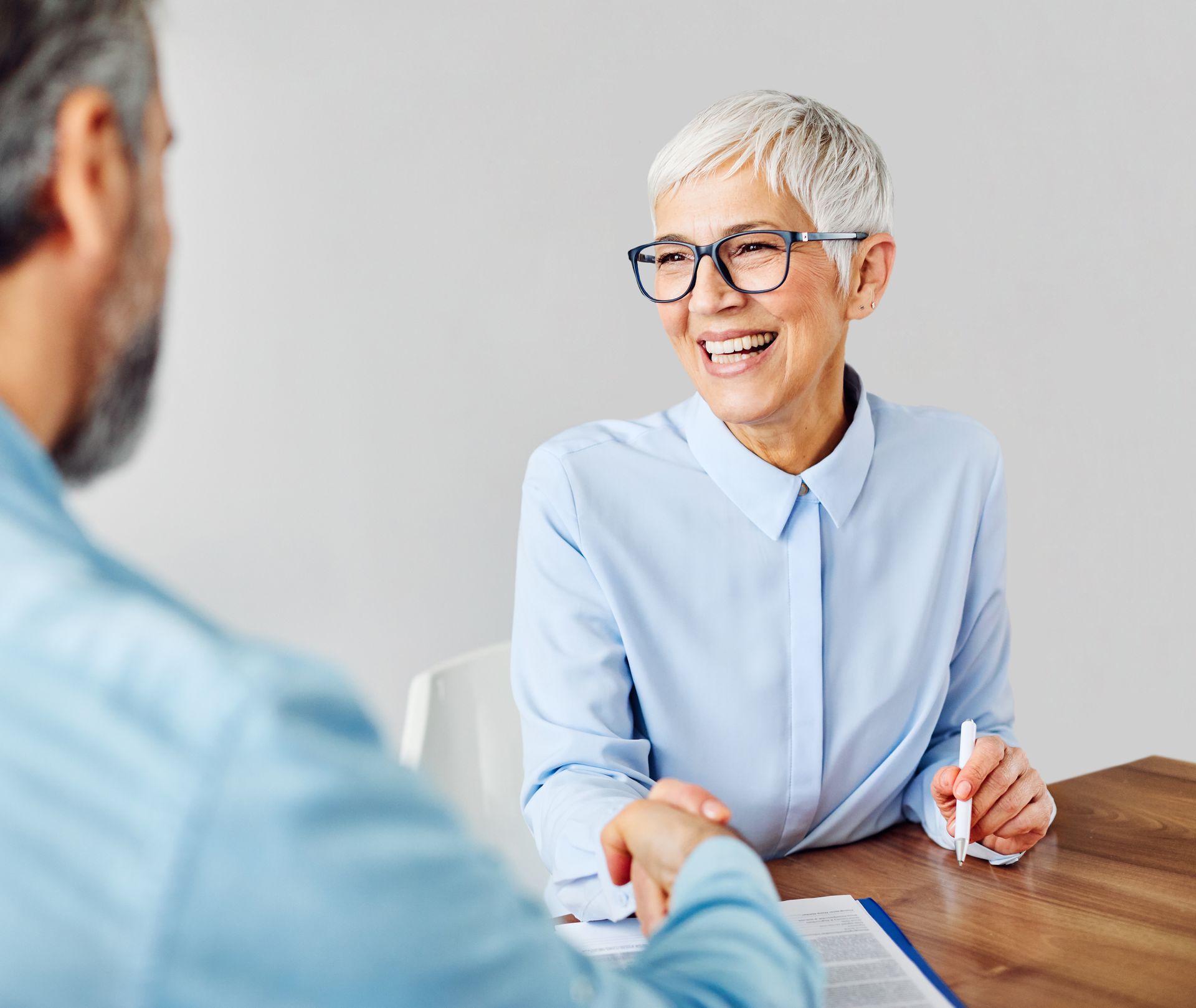 Two people in a bright office meeting, one smiling while taking notes across a wooden table.