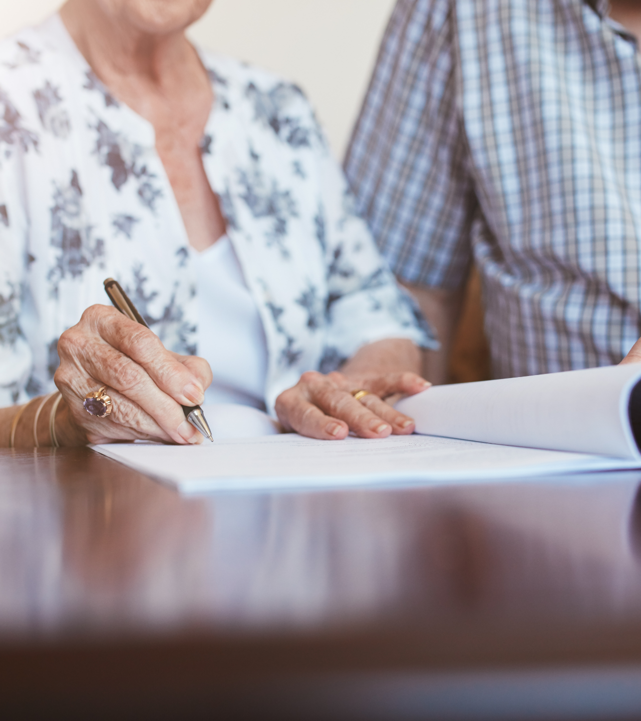 Two people signing documents at a table, one holding a pen over paper