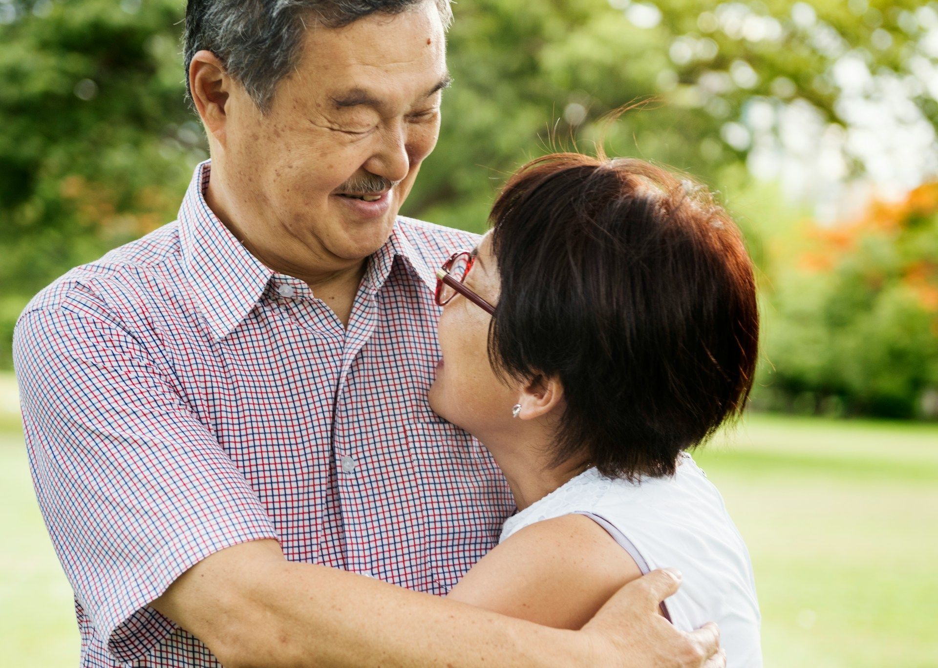 Two people smiling and embracing outdoors in a green park.
