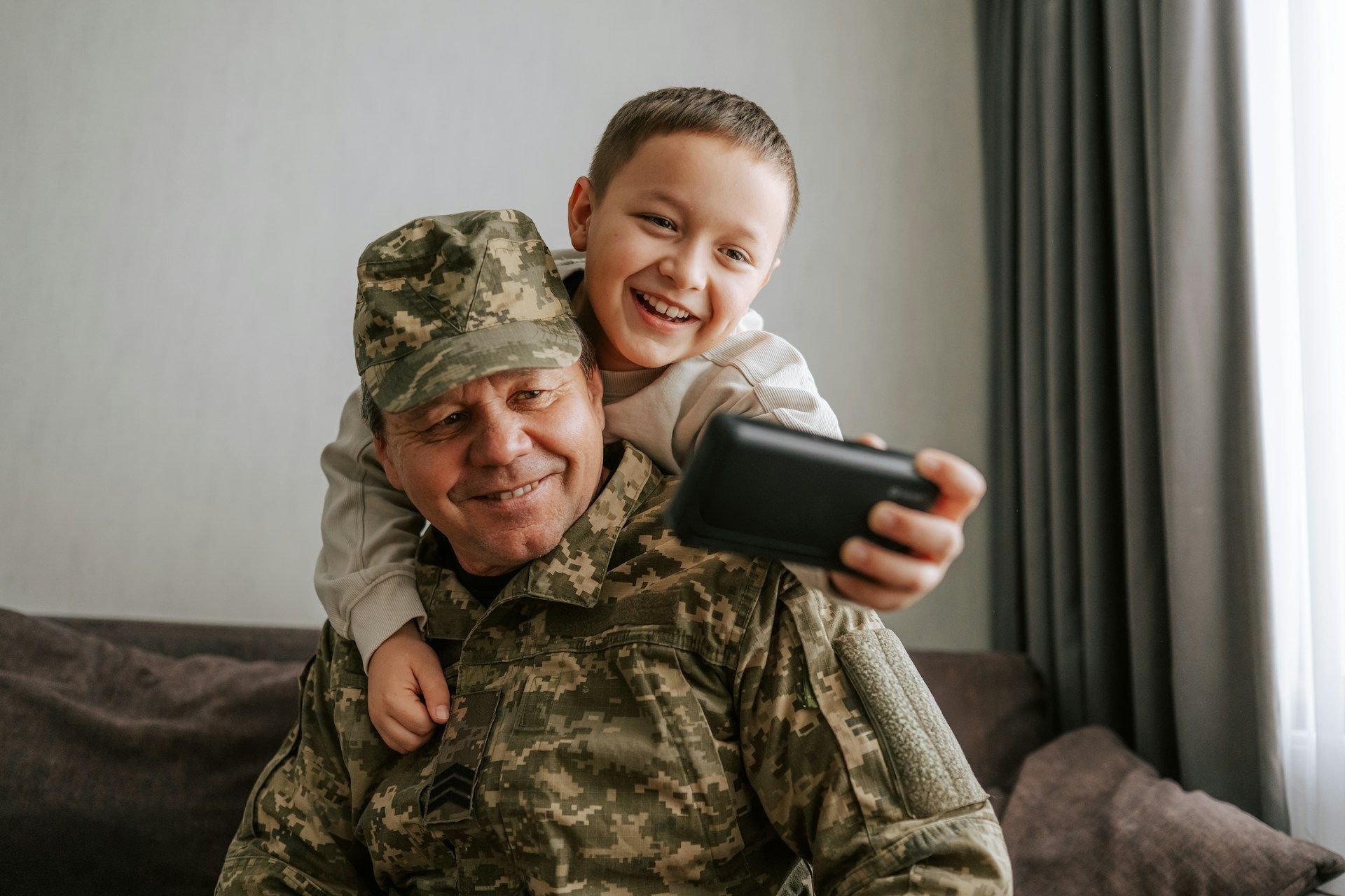 Soldier in camouflage smiling with a child taking a selfie on a couch