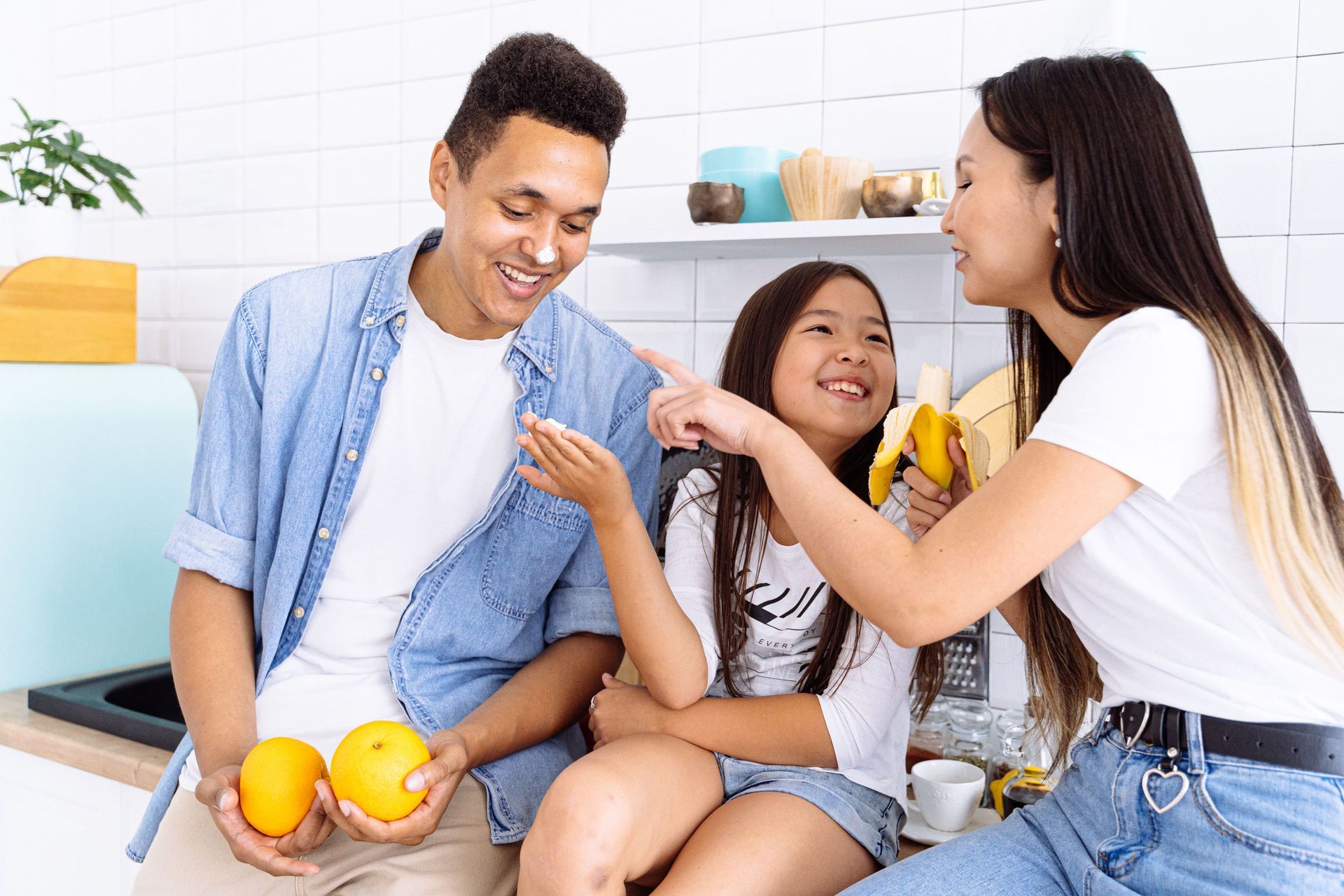 Three people sitting in a bright kitchen, smiling and sharing fruit on the counter