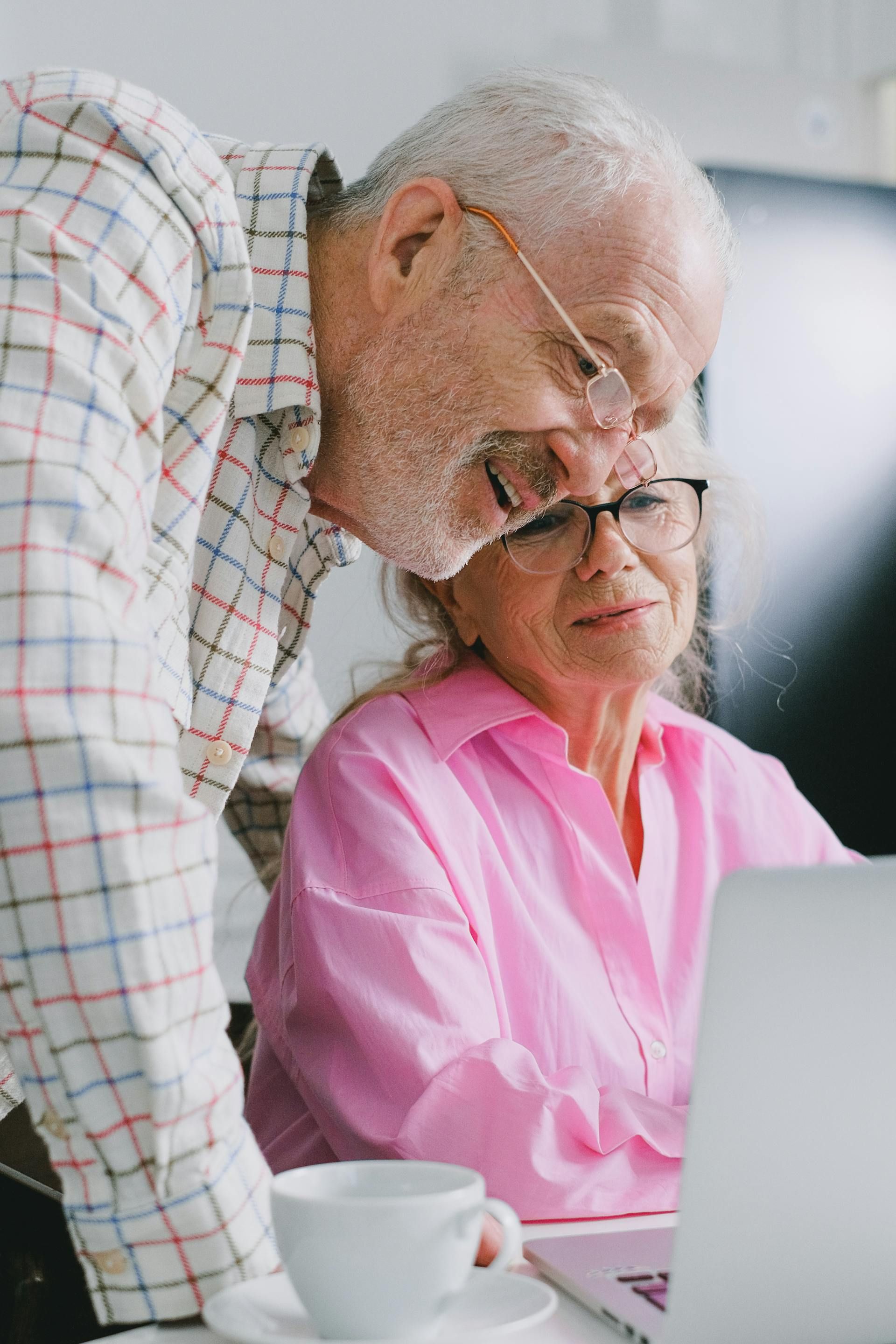 Older man and woman reviewing a laptop together at a table, with a coffee cup nearby.