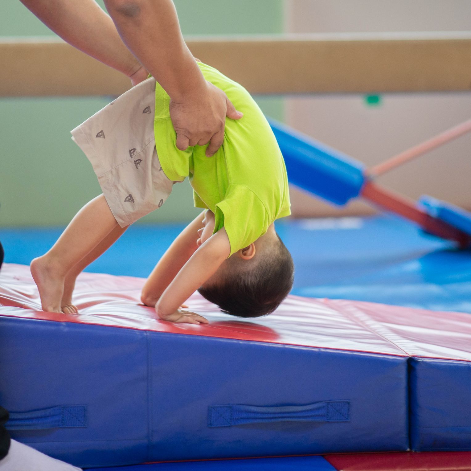 Child doing a backbend on a blue gym mat with an adult instructor assisting
