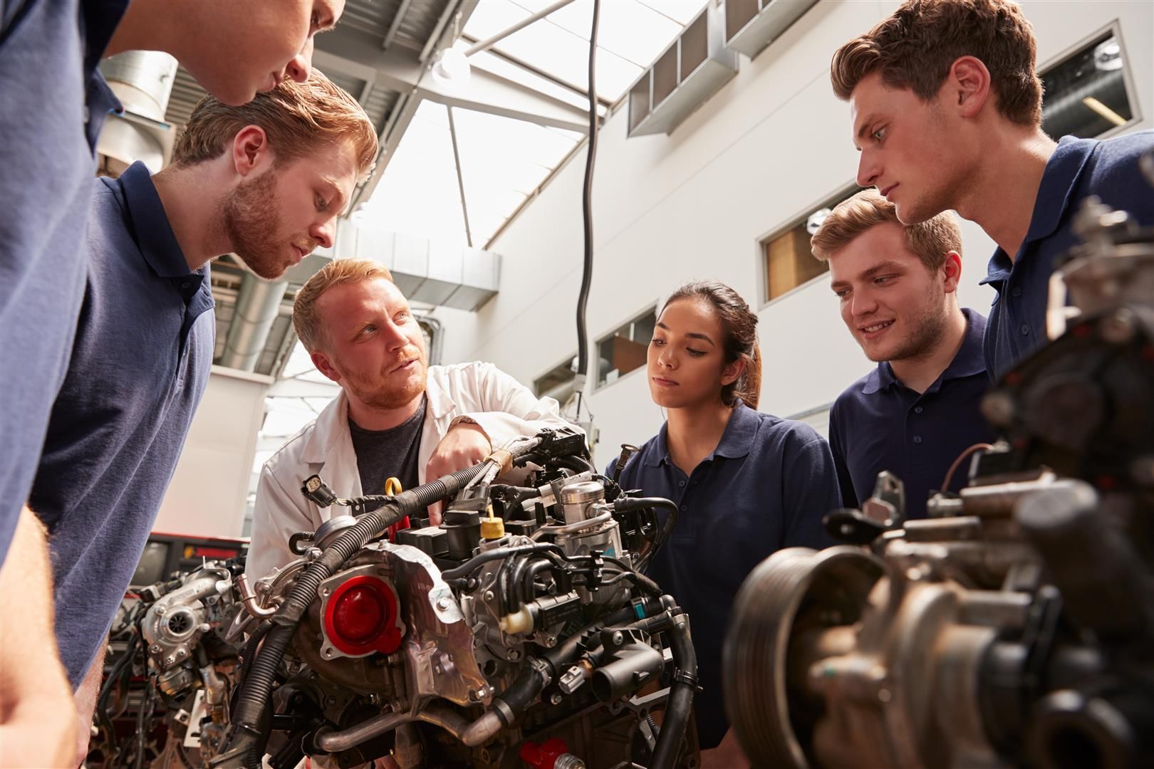 A group of people are looking at a car engine in a factory | Collins Automotive