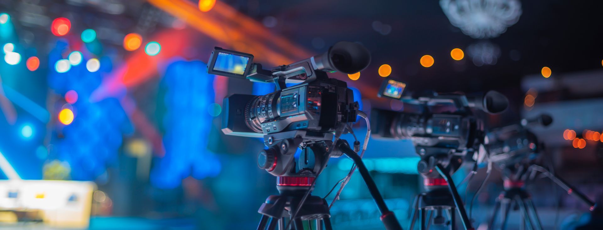 A row of video cameras are sitting on tripods in front of a stage.
