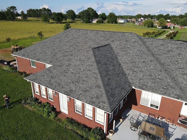 Aerial view of a large brick building with a gray shingled roof in a rural landscape