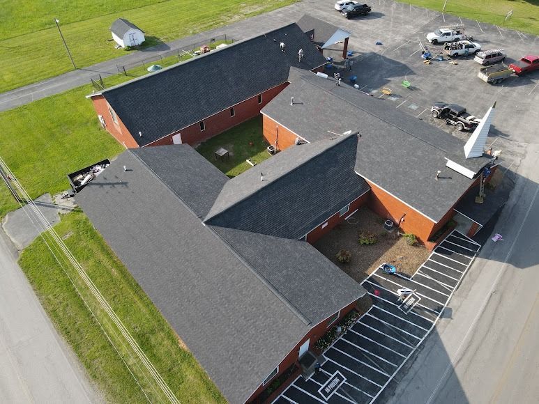 Aerial view of a red brick building with gray roofs, parking lot, and surrounding grassy fields.