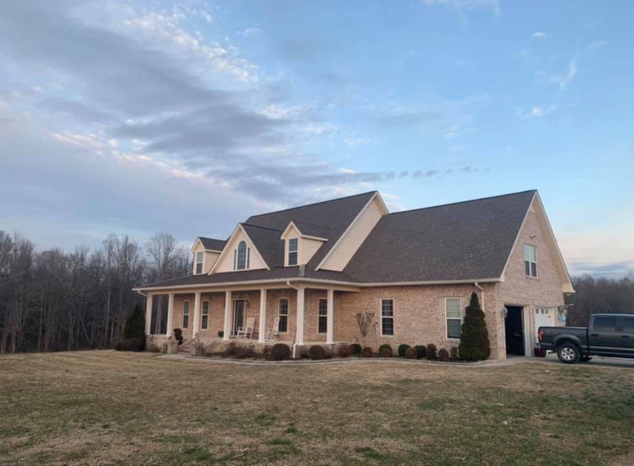 Large beige house with a covered porch and dark roof on a grassy lot at dusk