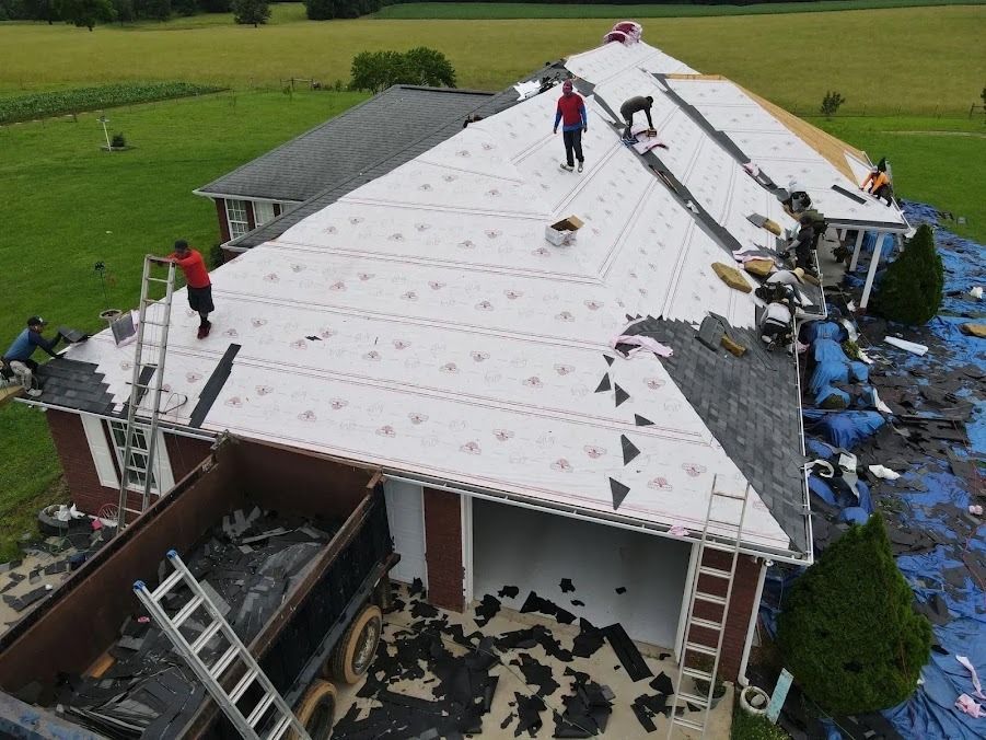 Workers replacing a large house roof with white underlayment and debris on the ground