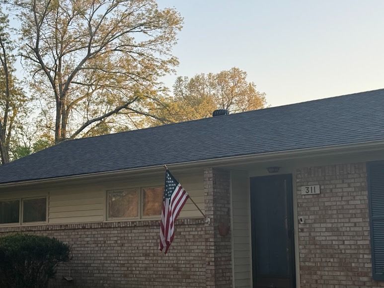 Single-story brick house with a dark roof and an American flag by the front door.