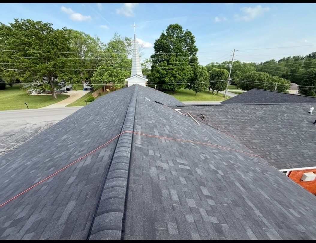 View from a rooftop with dark shingles, looking toward trees and a distant road under a clear sky