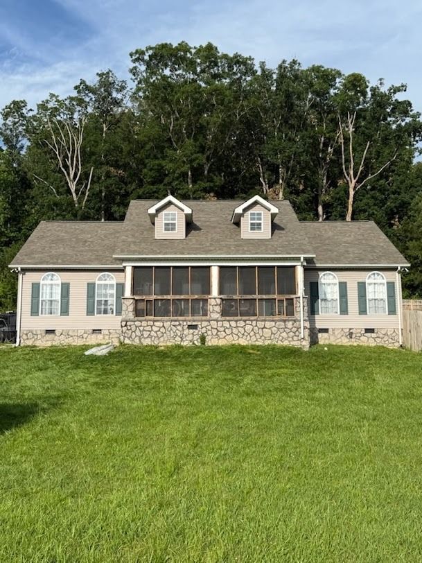 Stone house with gray roof and screened porch, set against trees and a grassy lawn.