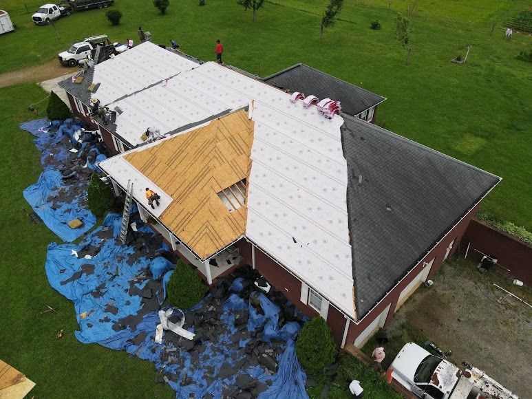 Aerial view of a roof with storm damage and tarps, debris scattered on the lawn.