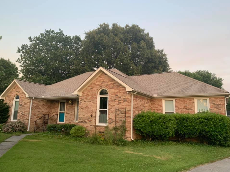 Single-story brick house with green lawn and trees at dusk