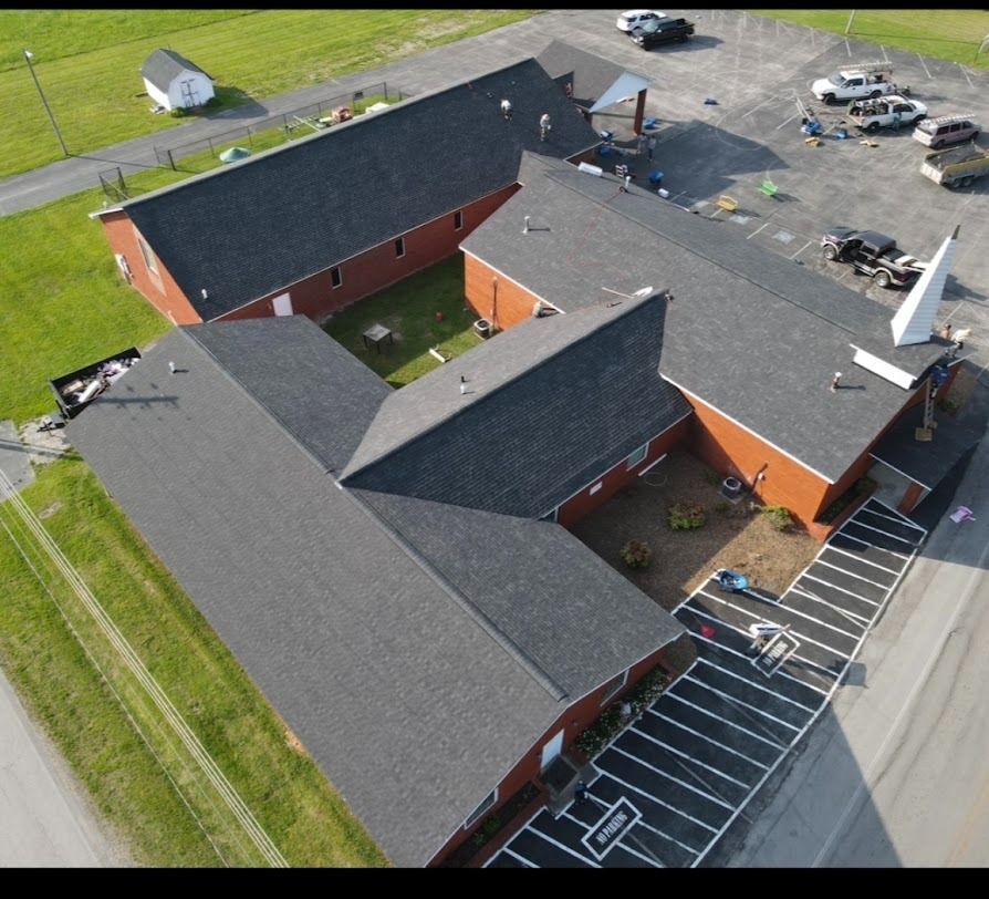 Aerial view of a red brick building complex with gray roofs, parking lots, and grassy areas.