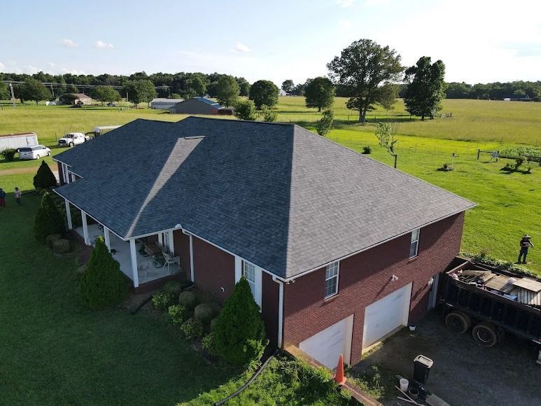 Aerial view of a red brick house with a gray roof in a green rural yard.