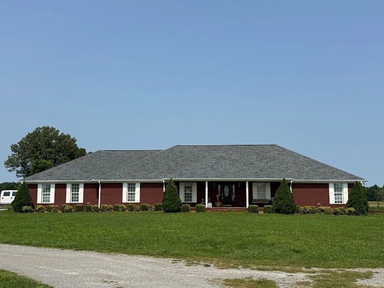 Single-story red brick house with a dark roof and wide front lawn under a clear blue sky