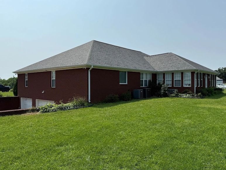 Red brick single-story house with gray roof on a green lawn under a clear sky