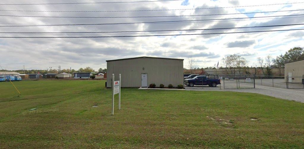 Grassy lot with a small beige utility building, parking area, and cloudy sky