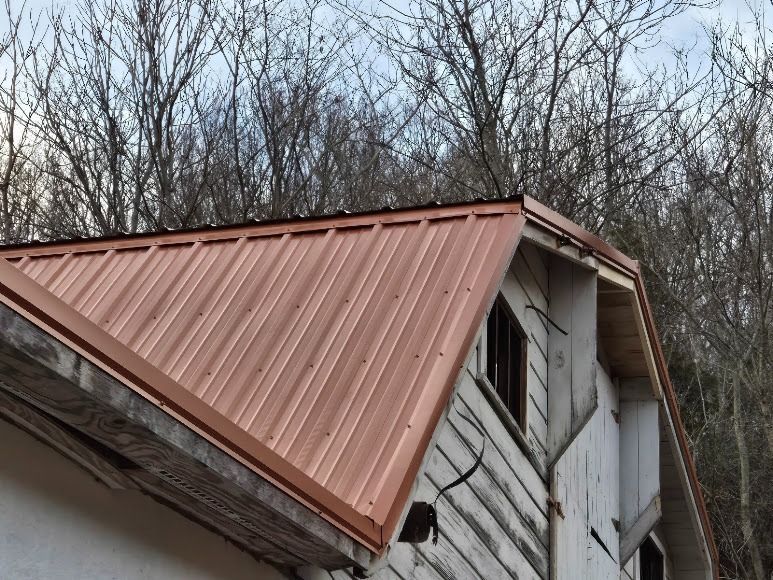 Damaged white house with a rust-colored metal roof and a leaning side wall near bare trees