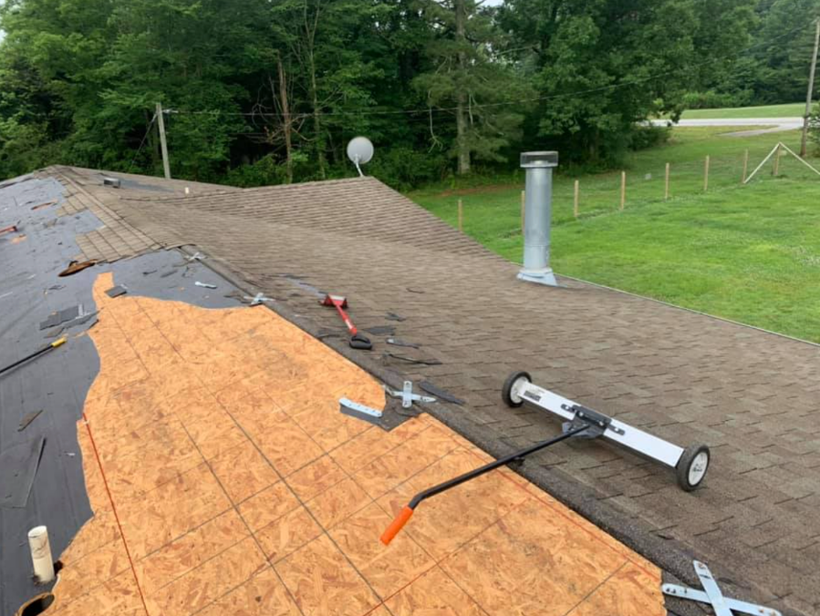 Roof repair with exposed plywood, shingles, tools, and a chimney on a house roof