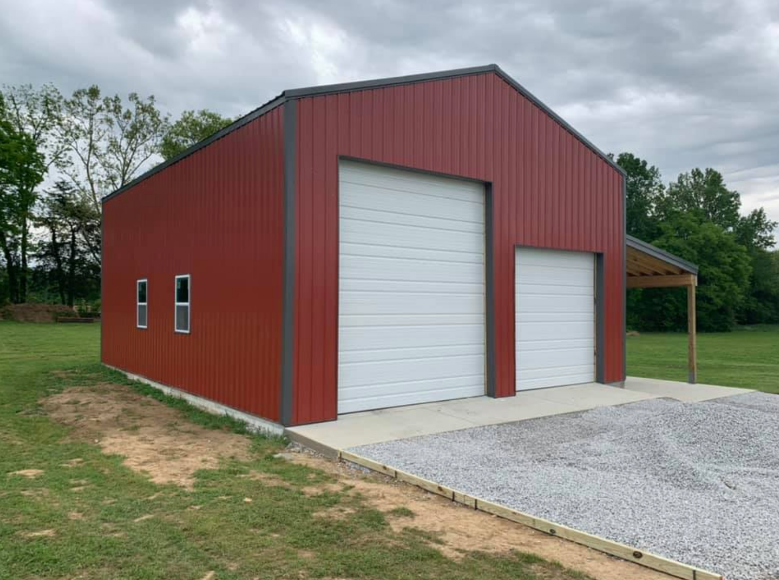 Red metal storage shed with two roll-up doors on a gravel pad under cloudy skies.