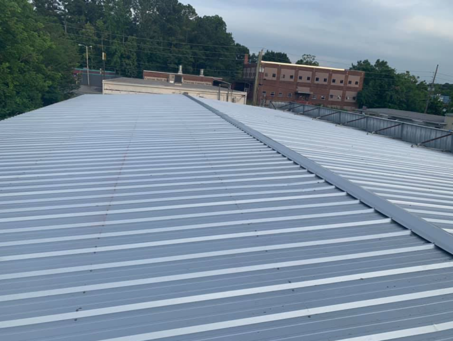 Rooftop with silver metal panels and vents, viewed toward trees and brick buildings in the distance