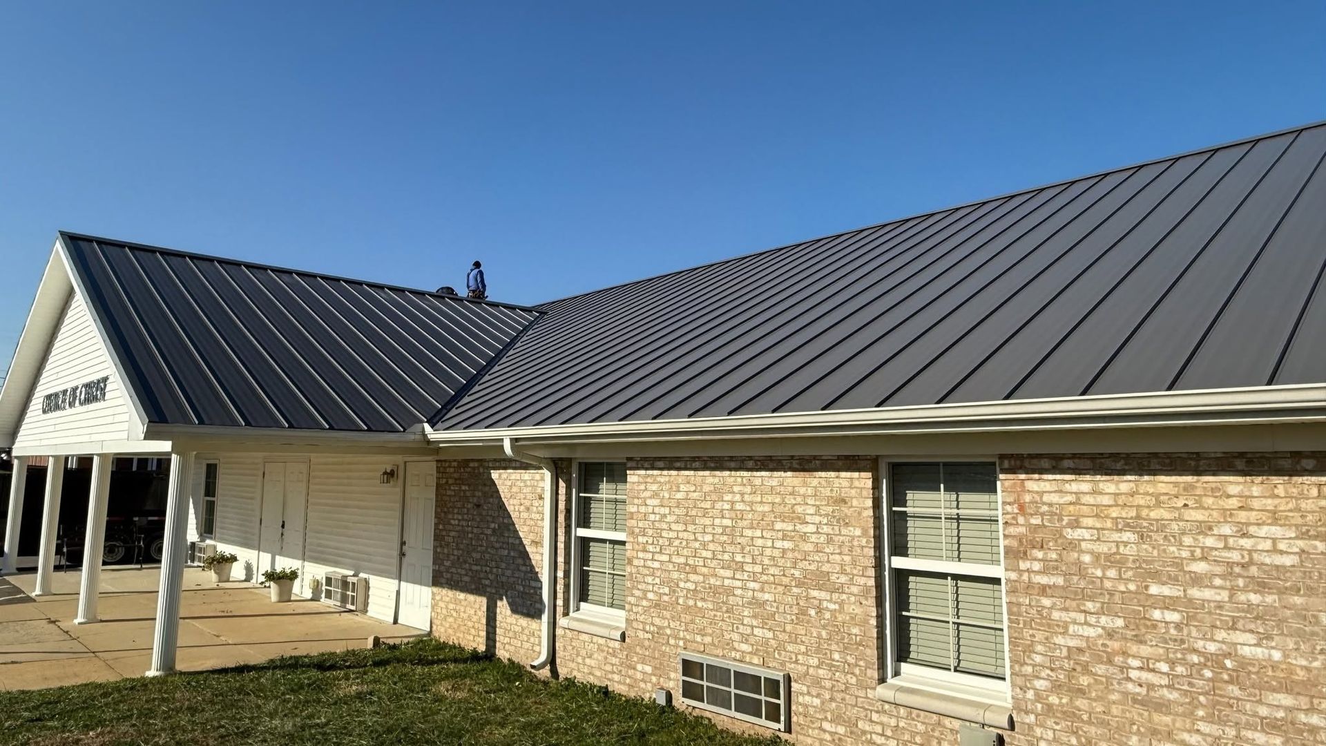 Brick building with a dark metal roof under a clear blue sky.