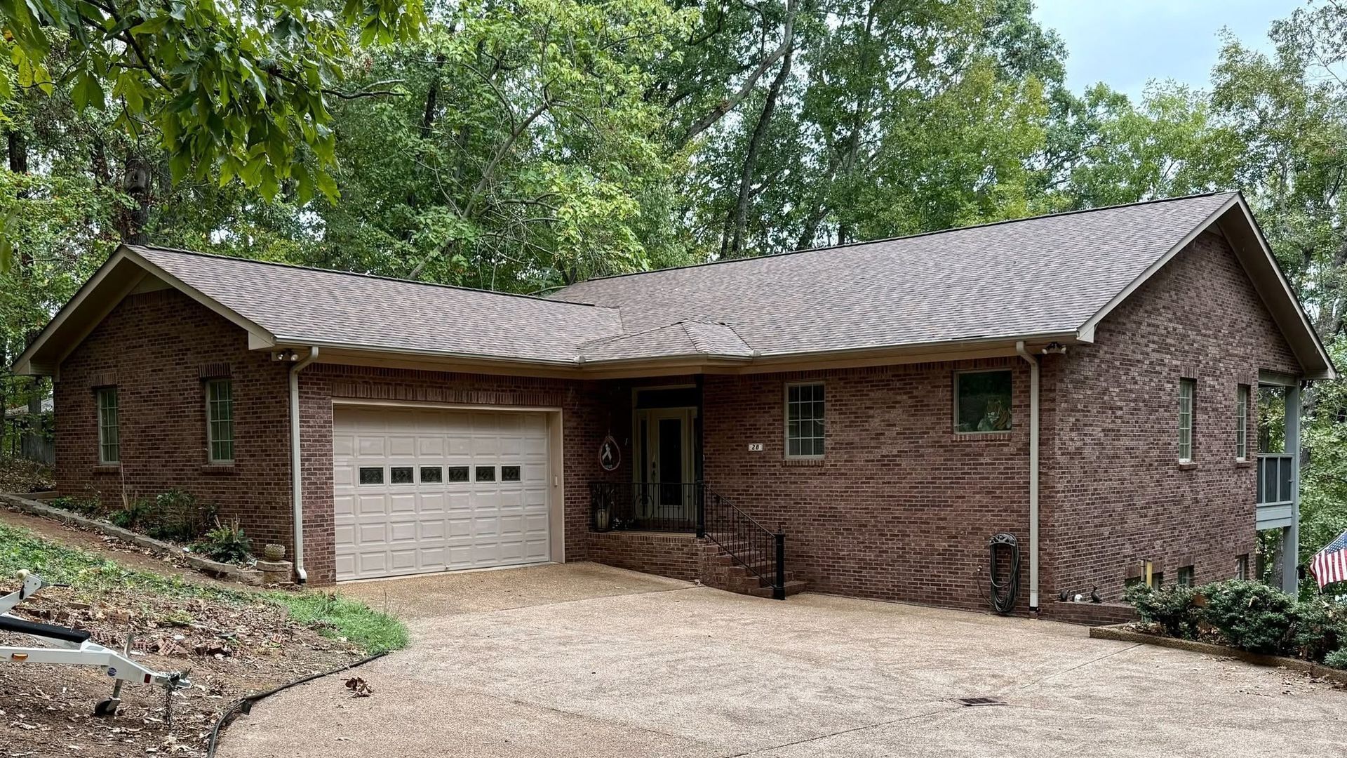 Brick house with attached garage and gravel driveway, surrounded by trees on a wooded slope