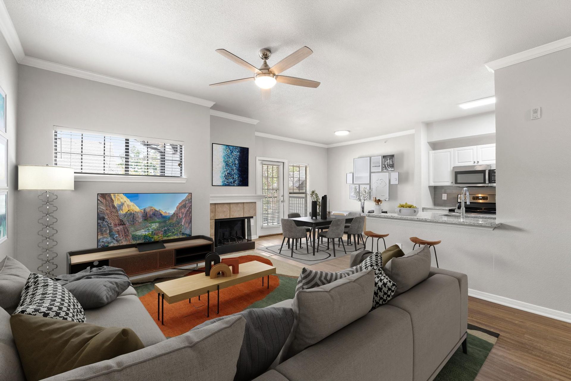 Bright open-plan living room with gray sofa, coffee table, TV, dining area, and white kitchen pass-through