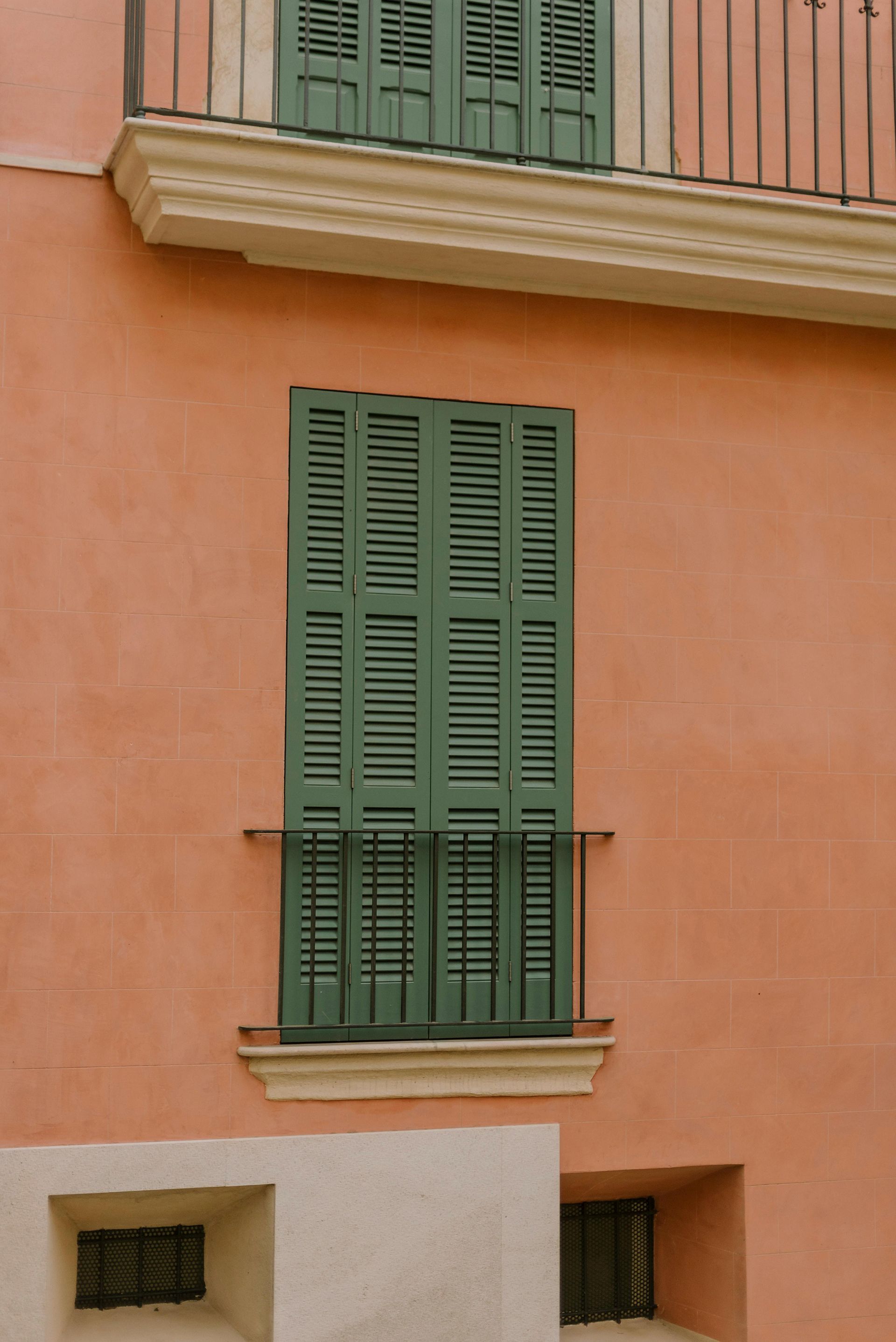 A window with green shutters on a pink building