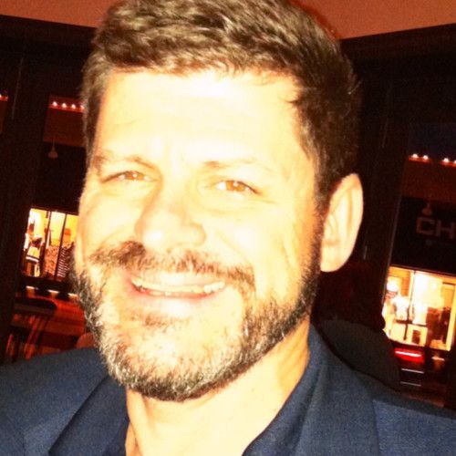 A man with a beard is smiling in front of a sign that says ch