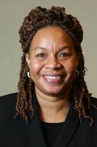 A woman with dreadlocks and earrings is smiling for the camera.