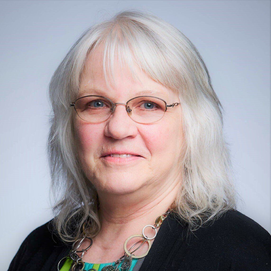 A woman wearing glasses and a black sweater looks at the camera