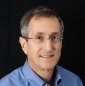 A man wearing glasses and a blue shirt is smiling for the camera.