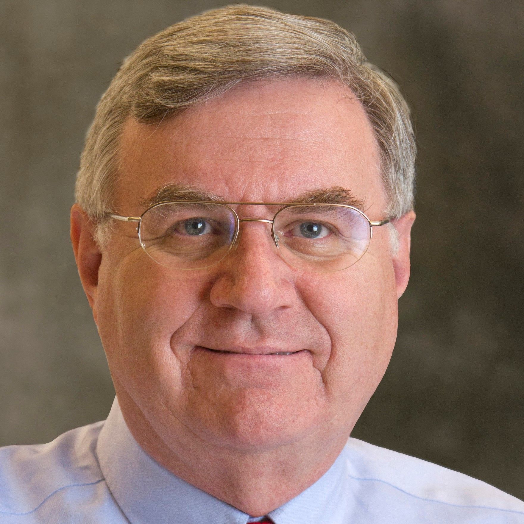 A man wearing glasses and a blue shirt smiles for the camera