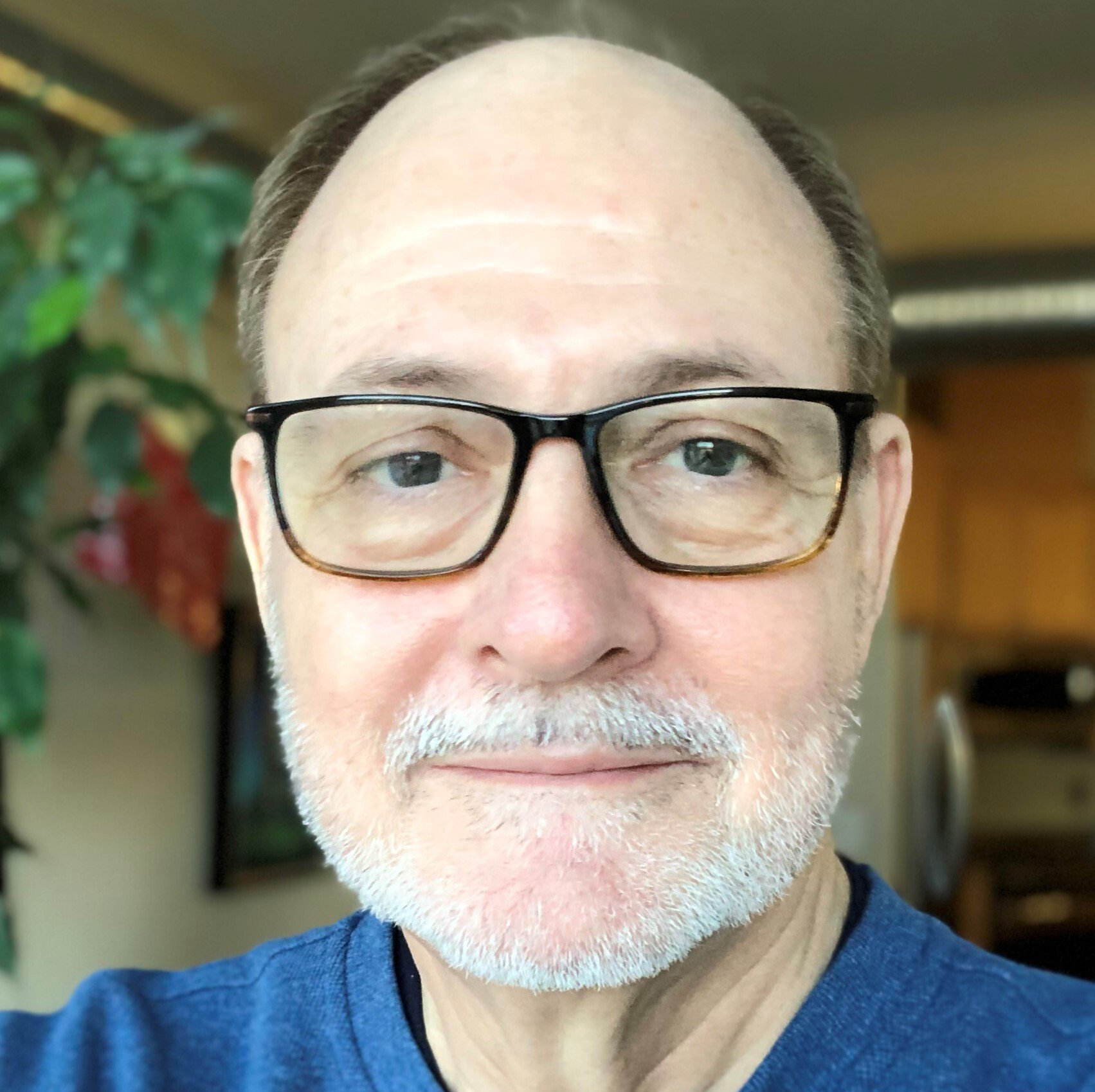 A man with glasses and a beard is wearing a blue shirt.