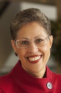 A woman wearing glasses and a red coat is smiling.