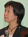 A woman with short black hair is wearing a black jacket and a necklace.
