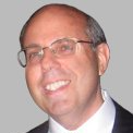 A bald man wearing glasses and a suit is smiling.