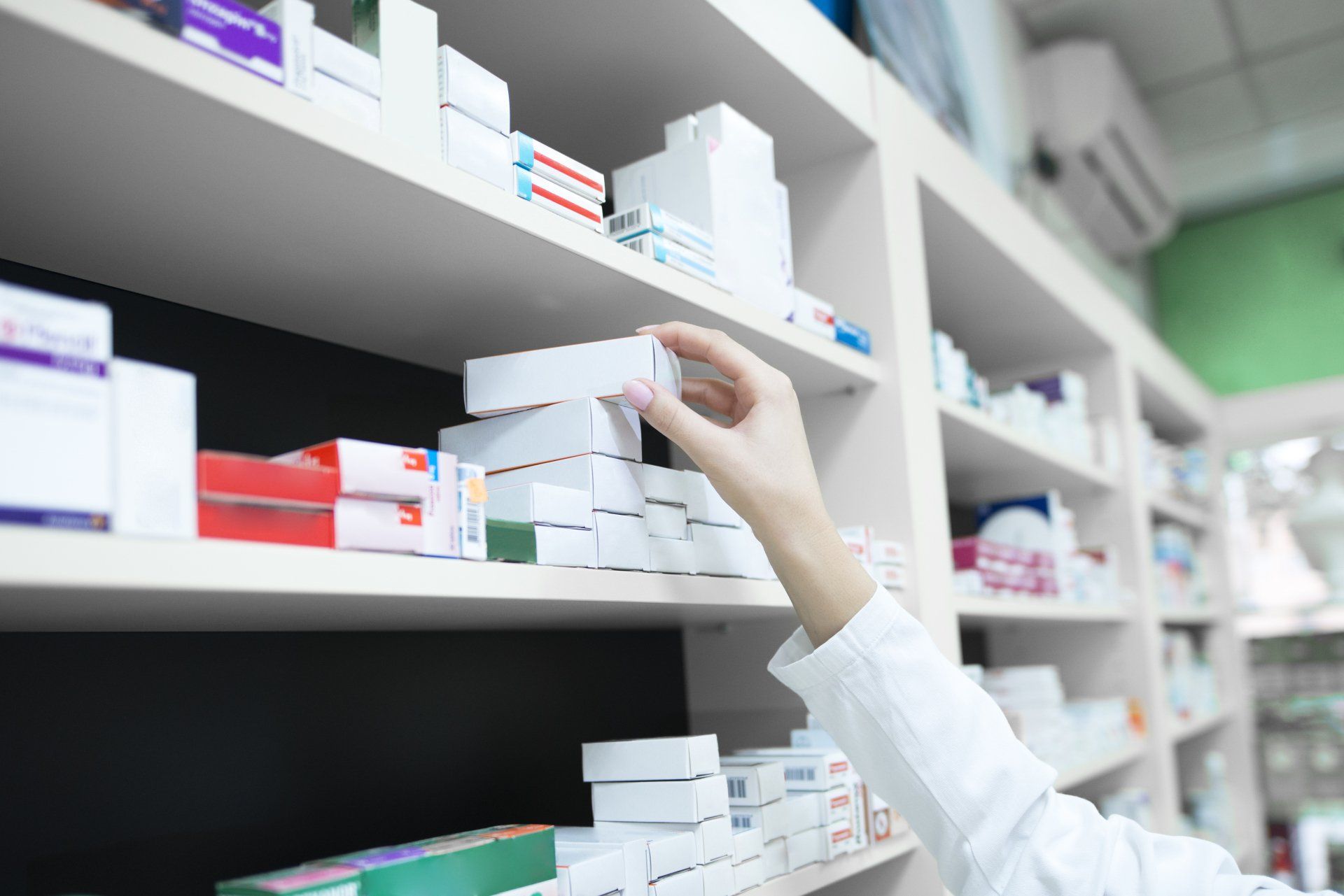 A pharmacist is reaching for a box of pills on a shelf in a pharmacy.
