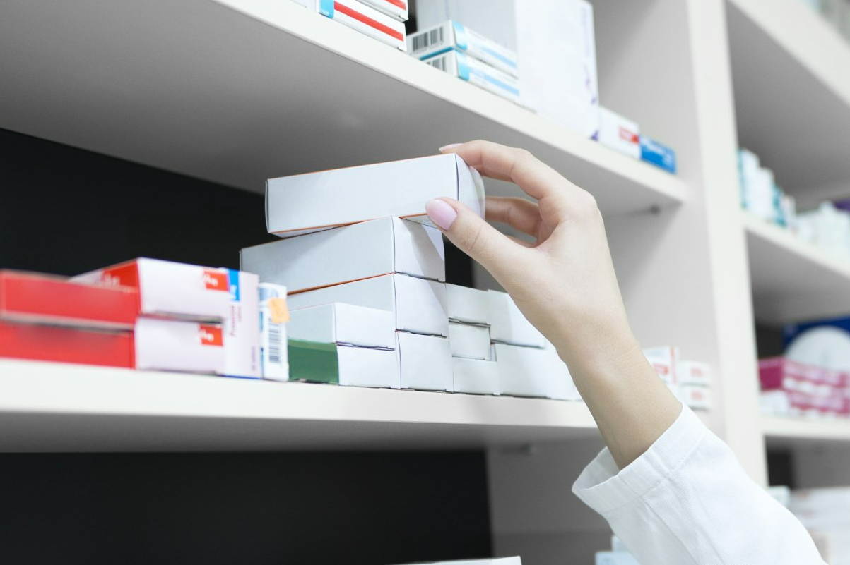 A person is reaching for a box on a shelf in a pharmacy.