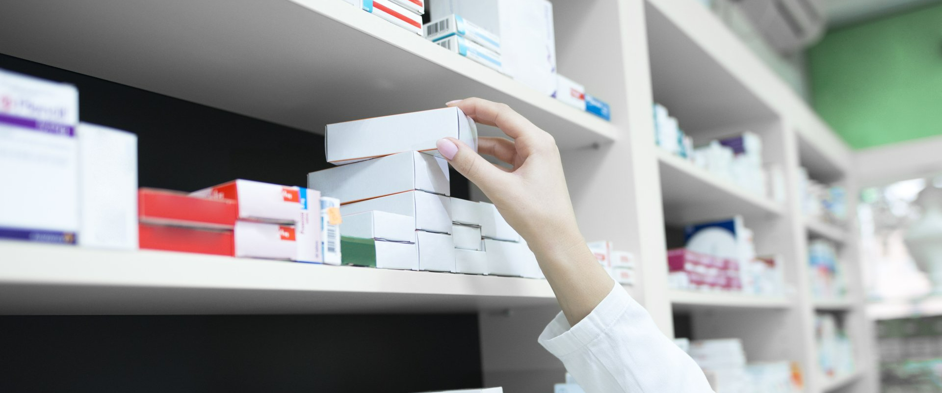 A person is reaching for a box of pills on a shelf in a pharmacy.